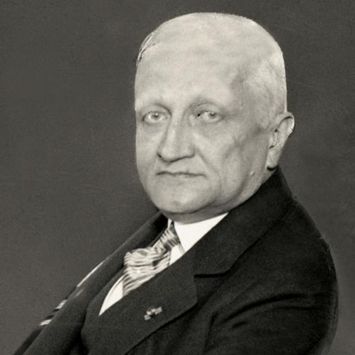 Konstanty Skirmunt - czarno-biały portret mężczyzny, siwe włosy, jasne oczy, ciemna marynarka, jasny krawat, biała koszula - półprofil.