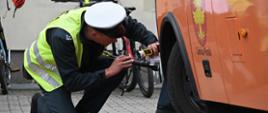 Kontrola stanu technicznego autobusu szkolnego. Inspektor transportu drogowego sprawdza połączenia układu kierowniczego i stan opon pojazdu.