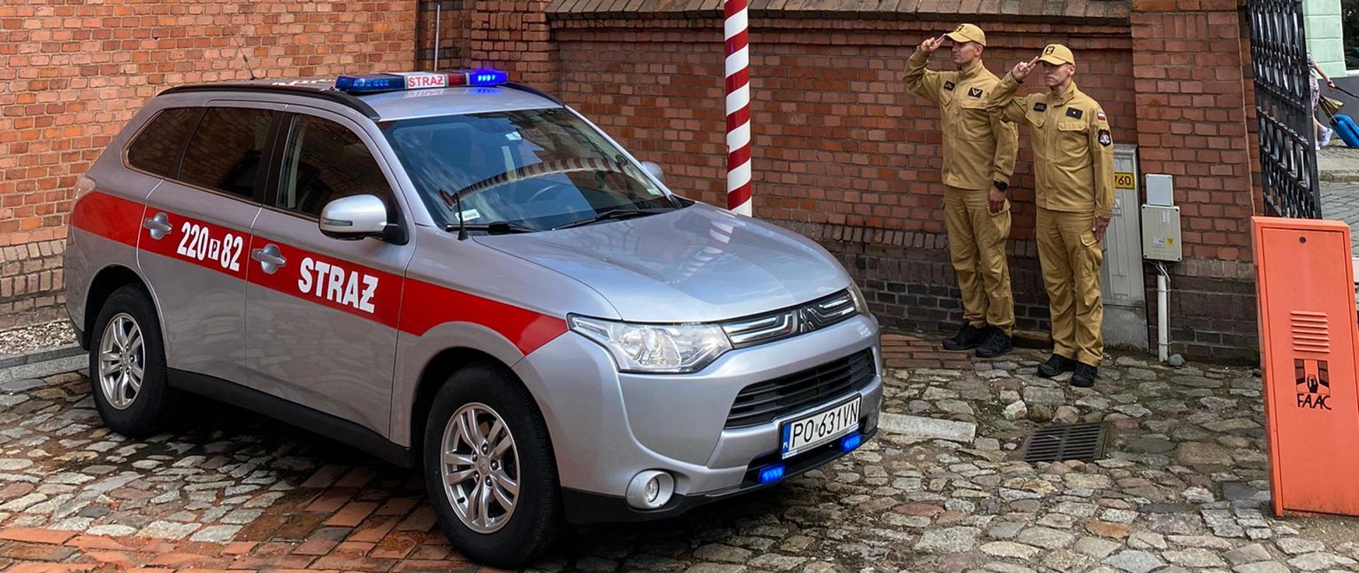 strażacy stoją prze remizą i samochodami strażacki oddając hołd bohaterom powstania warszawskiego
