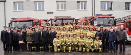 Zdjęcie przedstawia wszystkich zebranych funkcjonariuszy PSP oraz emerytów PSP, którzy uczestniczyli na uroczystej zmianie służby po przejściu na emeryturę Zastępcy Komendanta Miejskiego PSP w Rudzie Śląskiej st. bryg. Pawła Skwiry. W tle samochody pożarnicze i fasada budynku KM PSP w Rudzie Śląskiej.