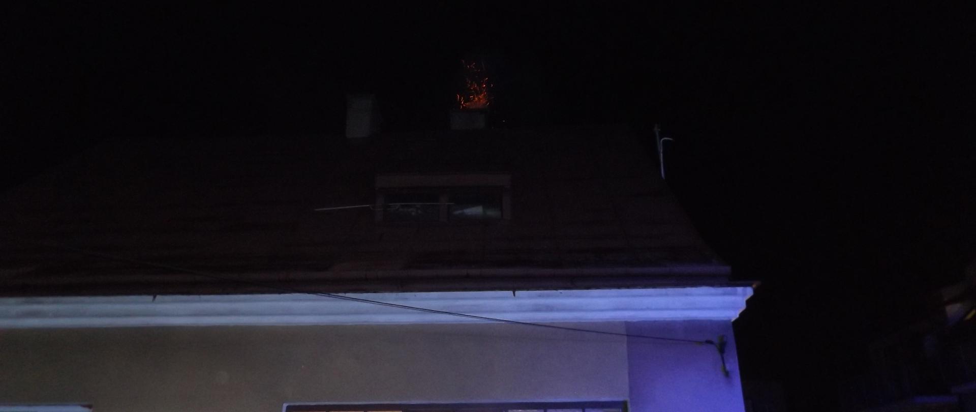 Na zdjęciu widzimy jednorodzinny budynek mieszkalny. Z komina sypią się iskry świadczące o pożarze sadzy w przewodzie kominowym