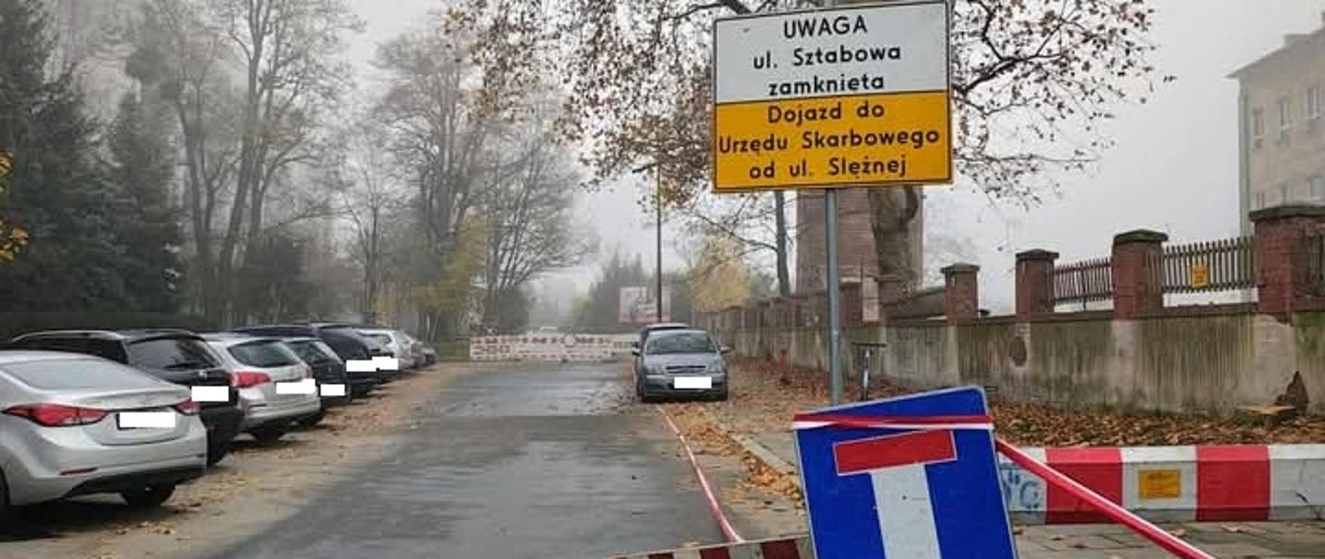 Na zdjęciu wyłączona z ruchu ulica. Na chodnikach stoją zaparkowane pojazdy 