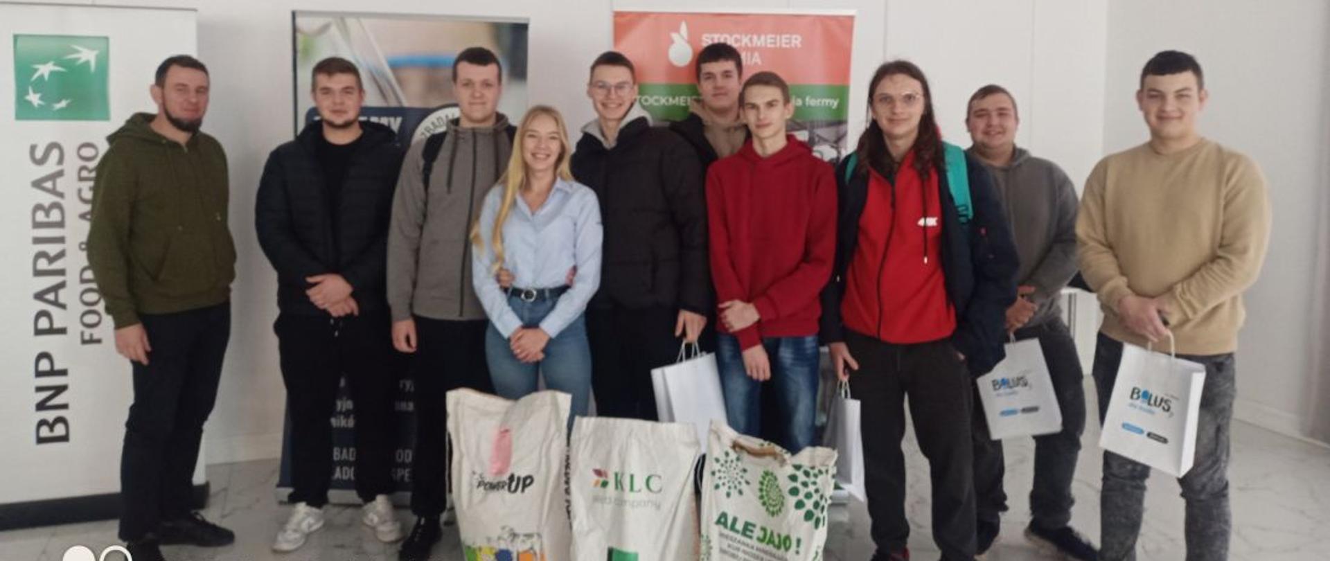 Grupa uczniów z opiekunami, przed nimi worki z paszą