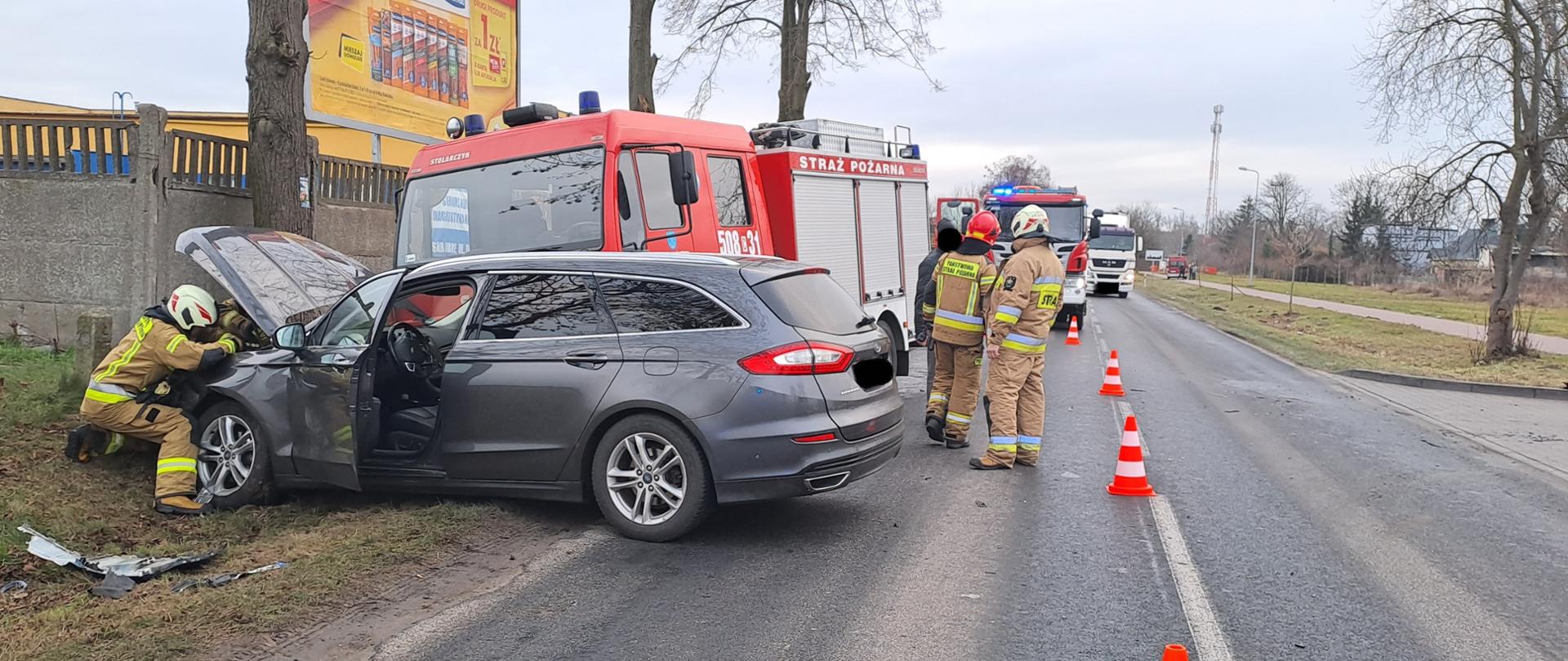 Zdjęcie przedstawia samochód osobowy oraz wóz strażacki po kolizji drogowej oraz strażaków PSP i OSP podczas prowadzonych działań.