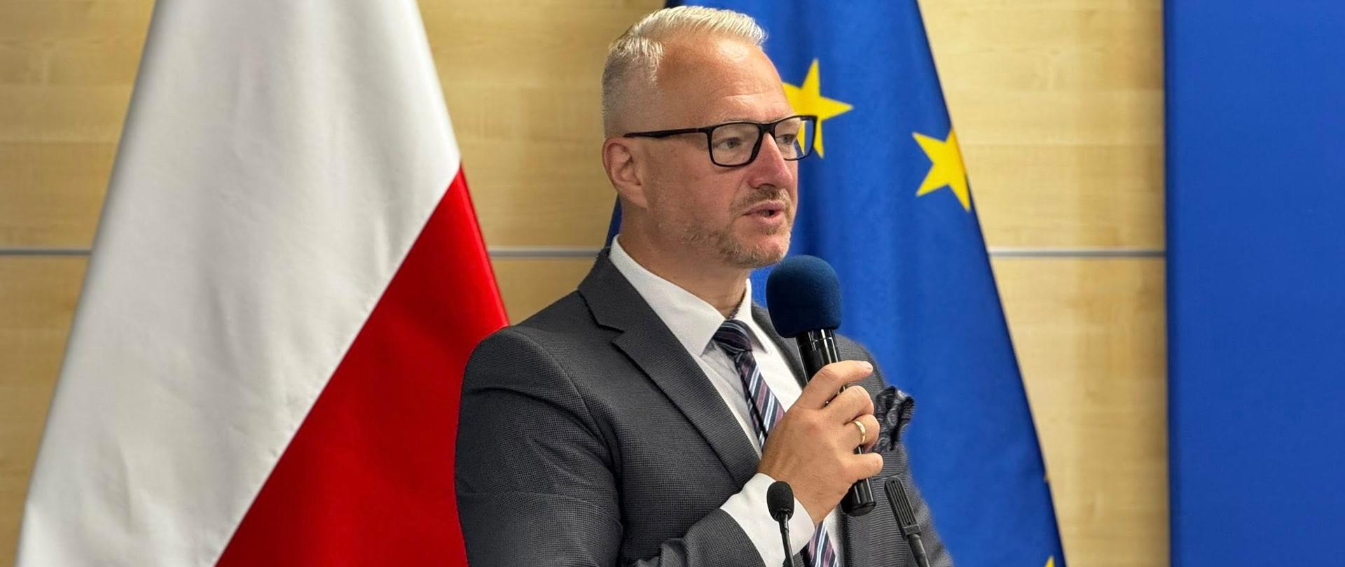 Mężczyzna w garniturze stoi i przemawia przez mikrofon 