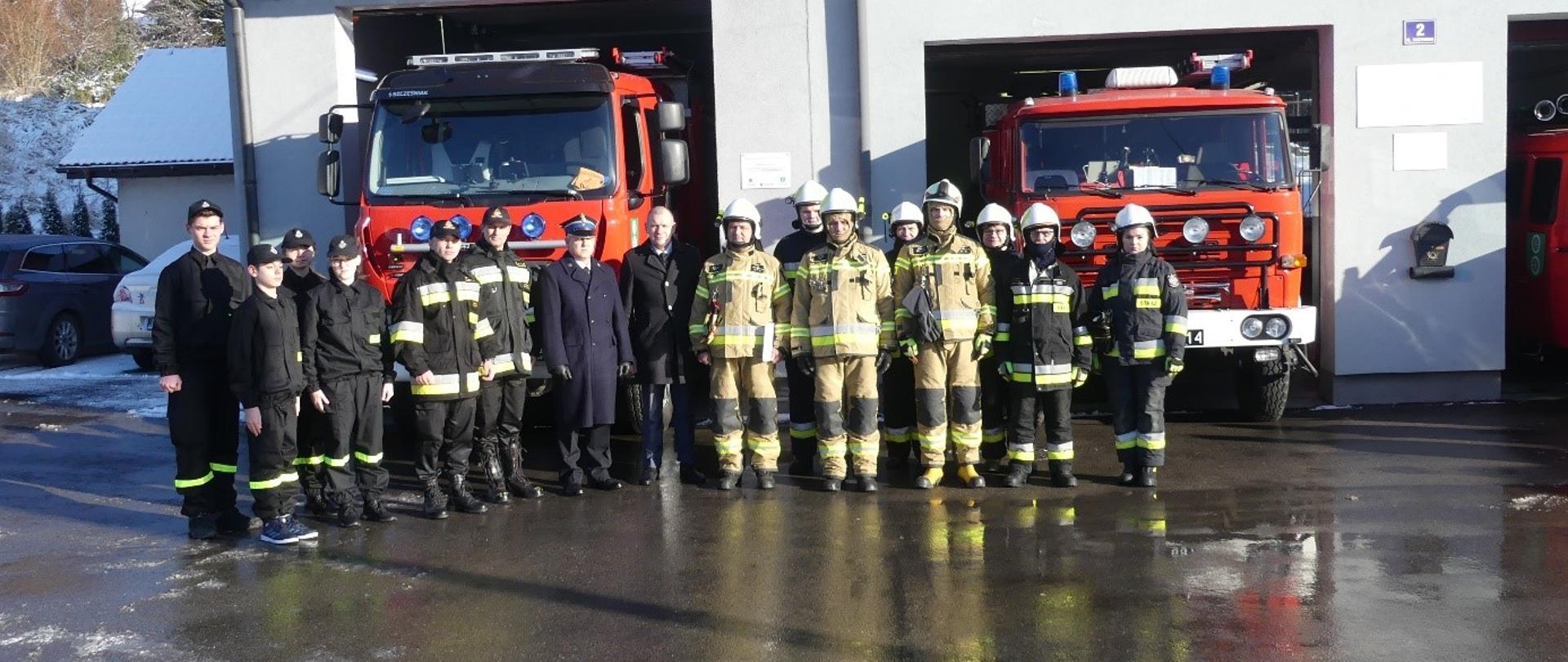 Strażacy z Polanki Wielkiej oraz funkcjonariusze PSP Oświęcim na tle remizy i pojazdów