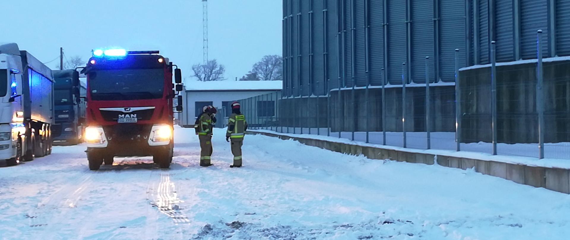 Strażacy stojący przy pojeździe ratowniczo-gaśniczym na terenie akcji