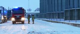 Strażacy stojący przy pojeździe ratowniczo-gaśniczym na terenie akcji