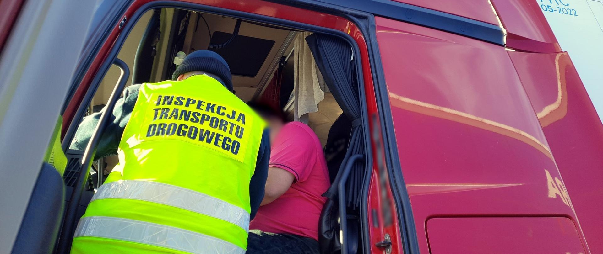 Inspektor wielkopolskiej ITD stoi w wejściu do kabiny ciężarówki i pobiera wymagane dokumenty od kierowcy.