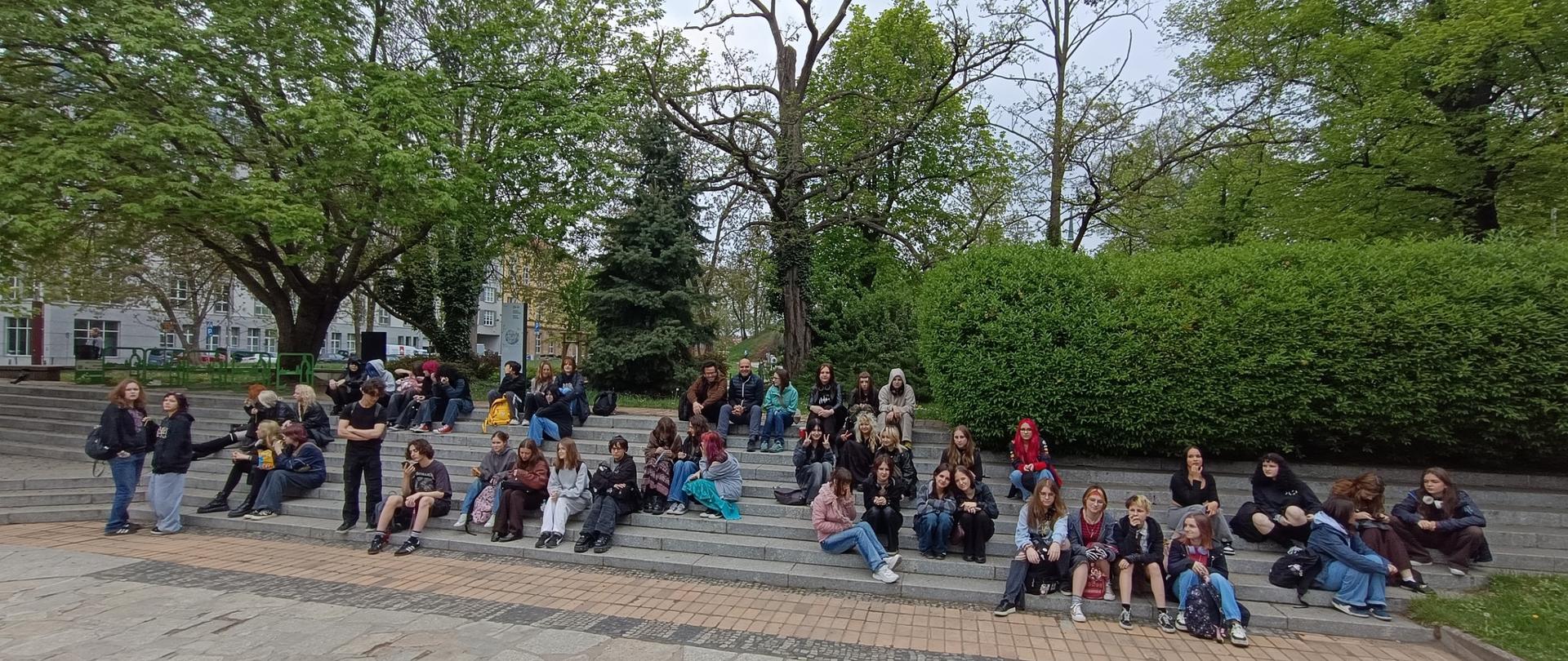 Grupa młodzieży siedzi na schodach, architektura i zieleń miejska