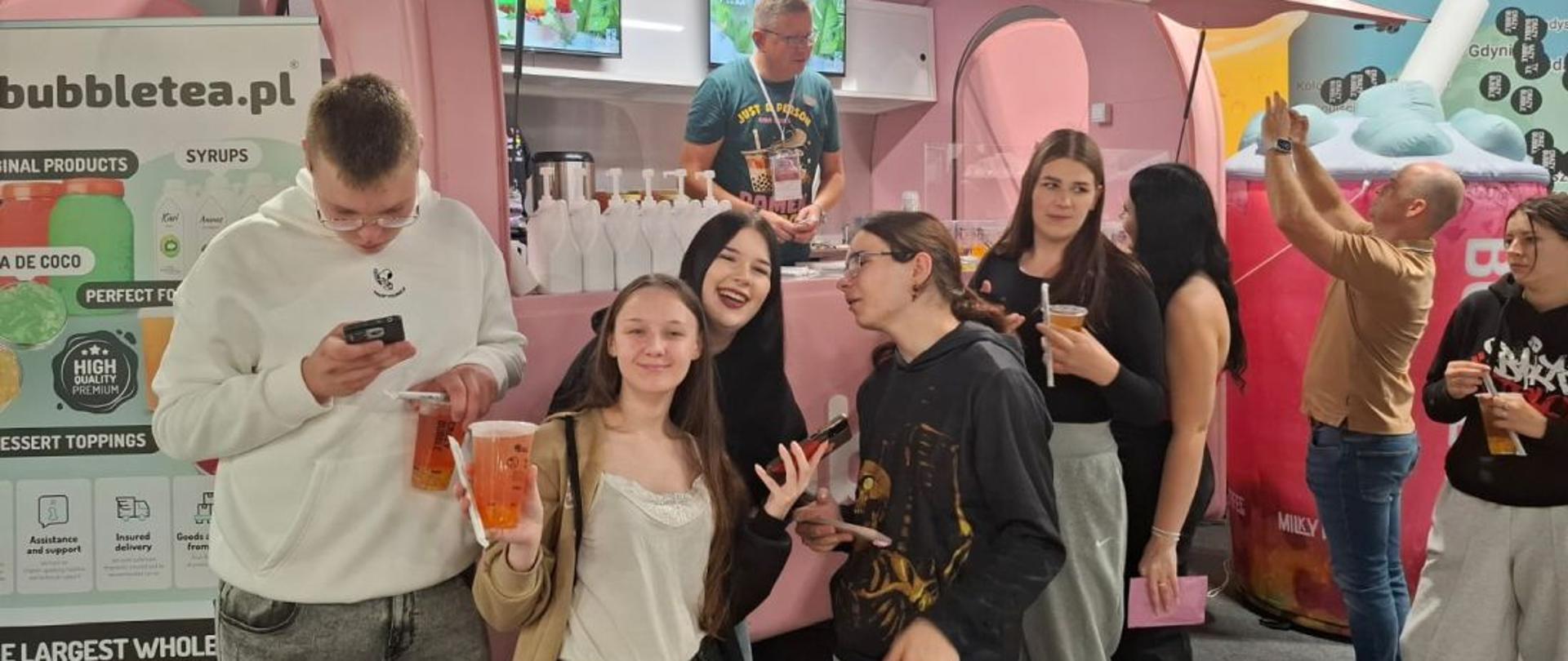 Grupa uśmiechniętych uczniów i uczennic z napojami przed stoiskiem z napisem "Crazy Bubble"