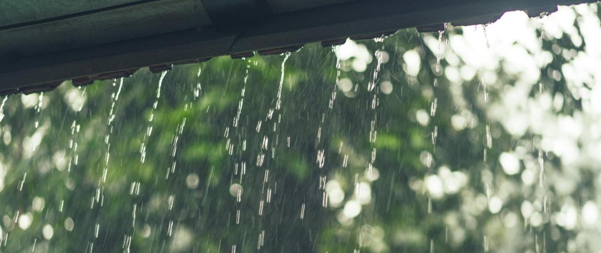 zdjecie kropli wody spływających z krawędzi dachu w trakcie opadów deszczu