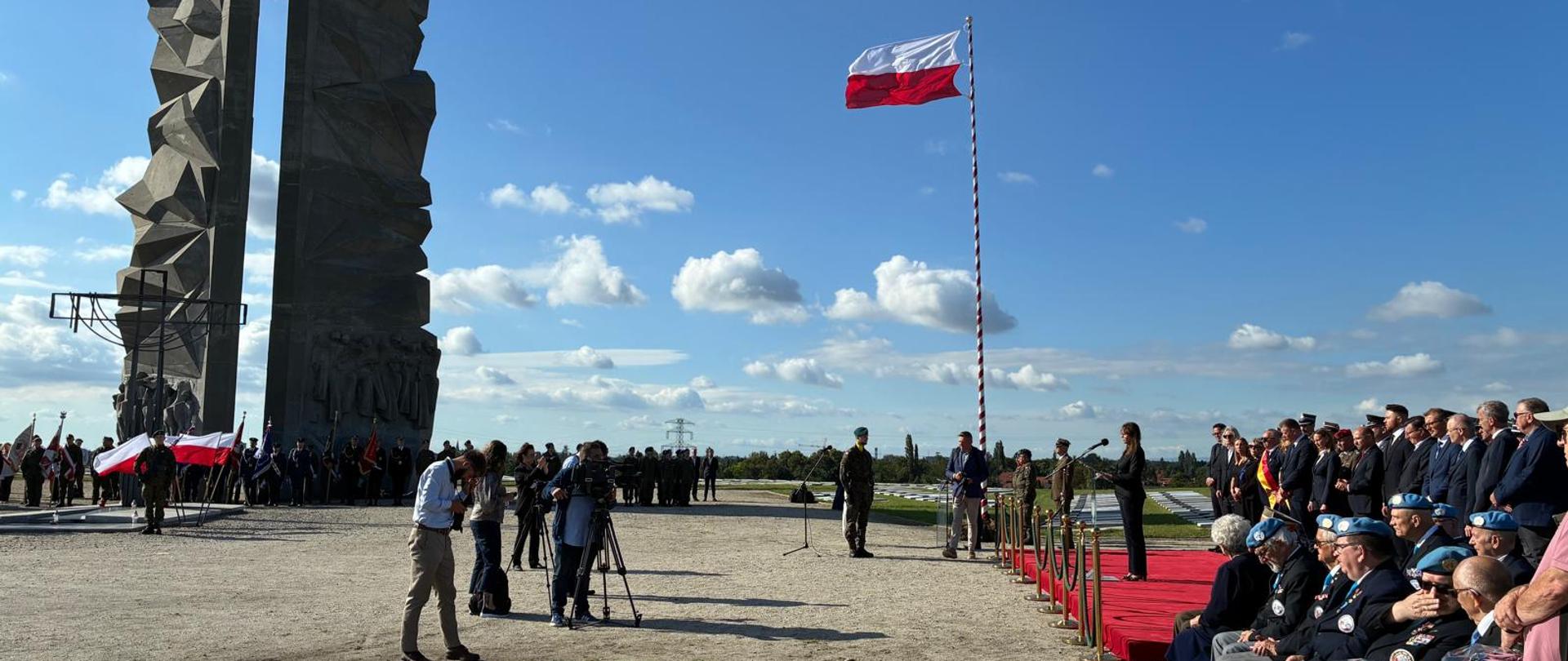 Uczestnicy wydarzenia wraz mówcą stojący przy pomniku.