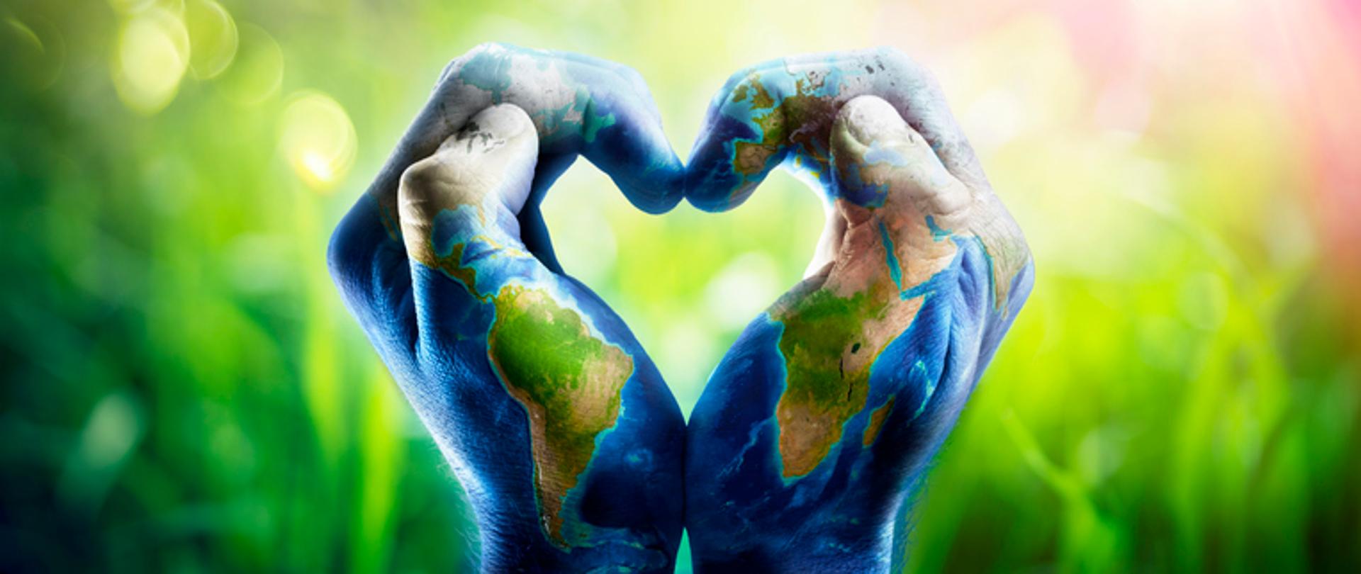 Ludzkie ręce kształtujące serce. Ręce są pomalowane, wzorzyste i przedstawiają mapę świata na tle z przewagą zieleni.