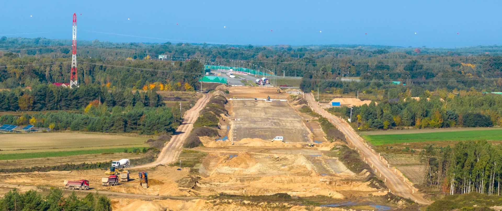 Widok na plac budowy autostrady A2. Wczesny etap prac. Widoczny szeroki pas oczyszczonej ziemi i przygotowanej podbudowy pod nową autostradę. W tle, na horyzoncie widoczne już gotowe pasy ruchu.