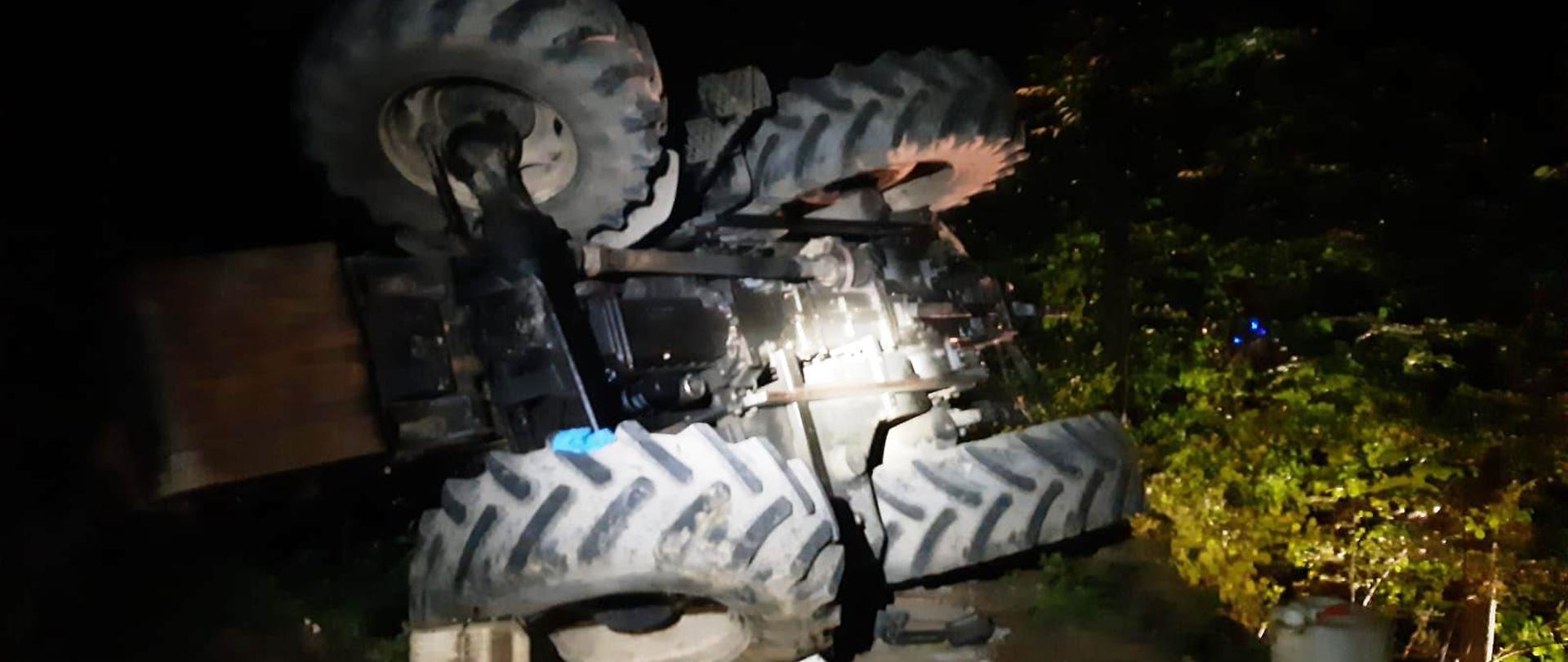 Leżący na boku ciągnik rolniczy. Obok niego płyny oraz pojemnik.