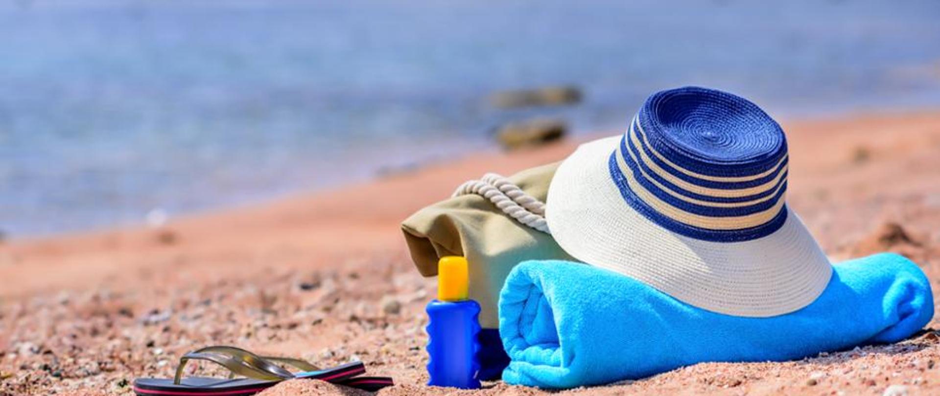 Plaża, klapek, kapelusz, zwinięty ręcznik i krem UV
