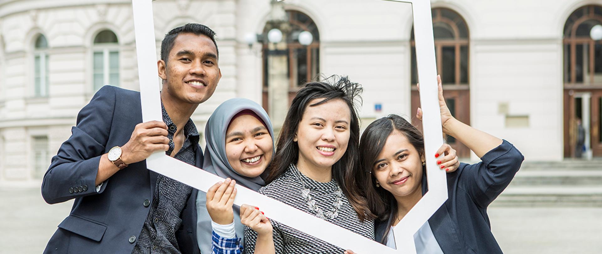 Studenci zagraniczni w Polsce trzymają wycięty kontur Polski, za nimi mury uczelni