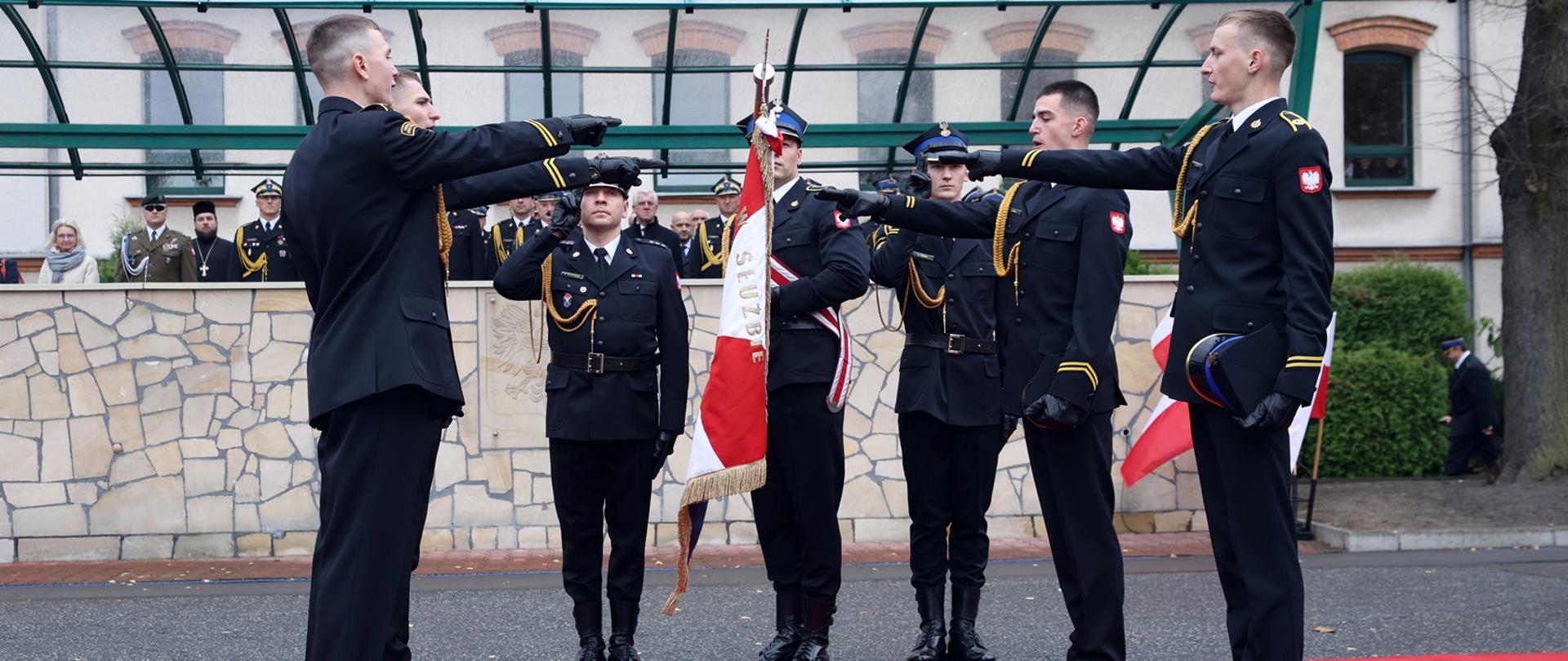 Czterech kadetów stoi na czerwonym dywanie z uniesioną wyprostowaną prawą ręką i składa ślubowanie na sztandar Centralnej Szkoły Państwowej Straży Pożarnej w Częstochowie