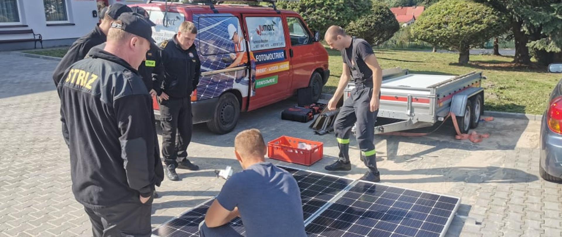 Zdjęcie przedstawia strażaków podczas szkolenia z instalacji fotowoltaicznej, które odbywa się przed remizą OSP Połczyn-Zdrój. Strażacy słuchają wykładu specjalisty od instalacji fotowoltaicznych..