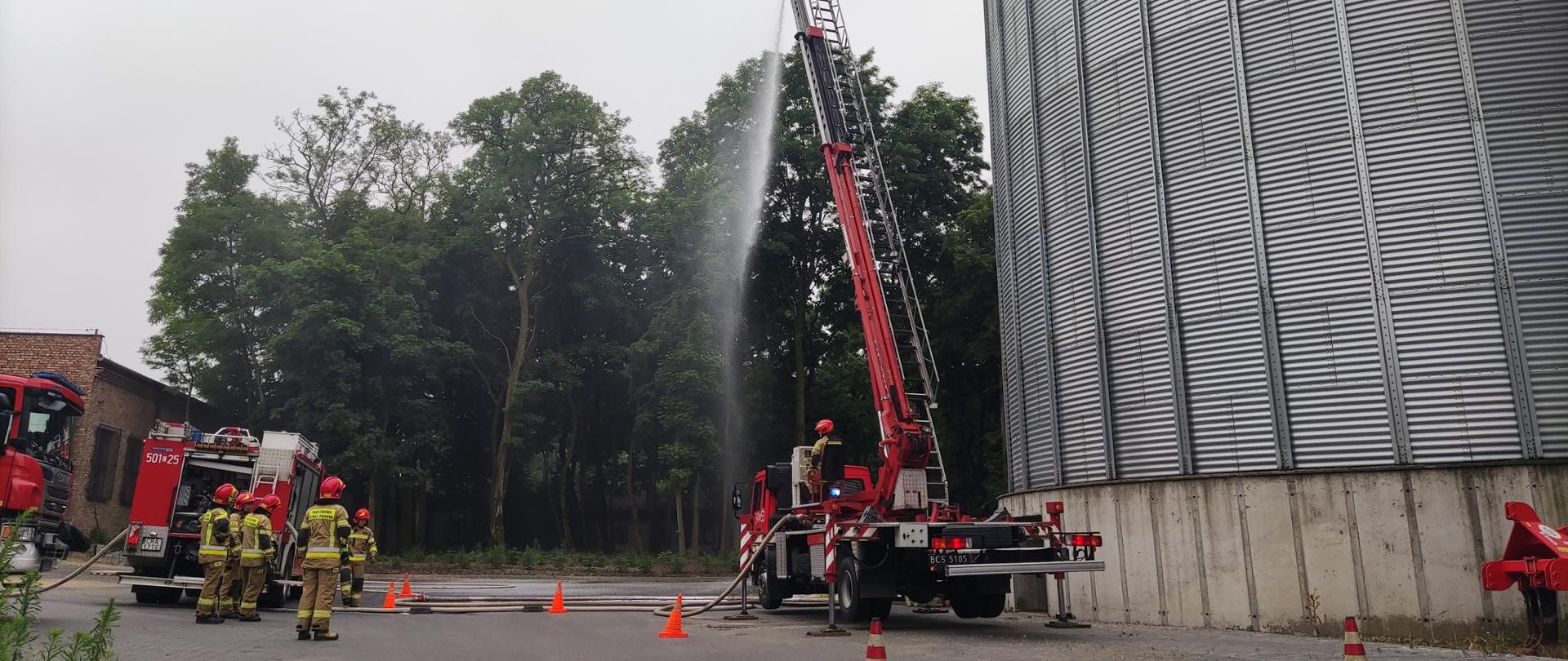 Zdjęcie przedstawia dwa pojazdy gaśnicze oraz podnośnik hydrauliczny podczas ćwiczeń obiektowych na terenie zakładu Młyn Gospodarczy w Dobrem