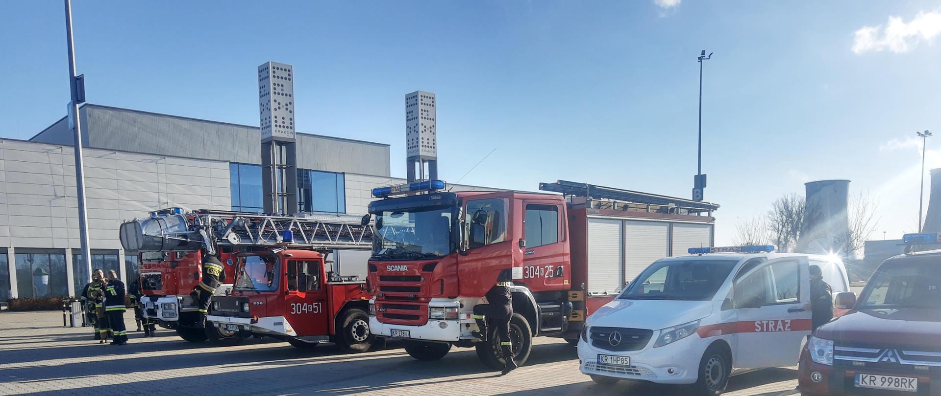 Zdjęcie przedstawia pojazdy pożarnicze na parkingu z kostki brukowej przed halą expo Kraków.