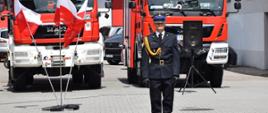 Na pierwszym planie dowódca uroczystości a za nim samochody gaśnicze i flaga państwowa