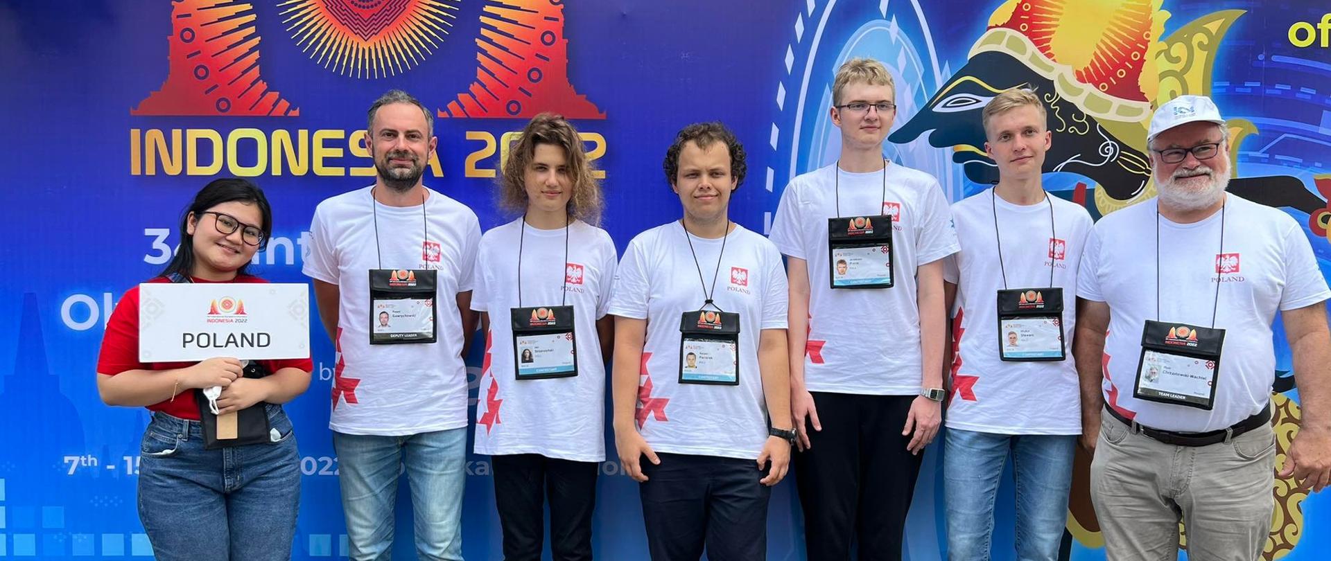 Polska delegacja - siedmioro młodych ludzi w białych koszulkach stoi pod niebieską ścianą.