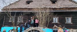 Kilkanaście osób wchodzi do zabytkowej chaty drewnianej