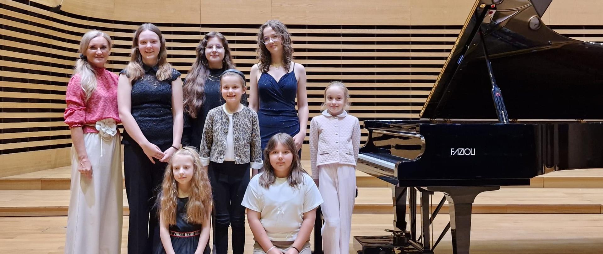 Siedem uczennic stoi na scenie razem z nauczycielką.