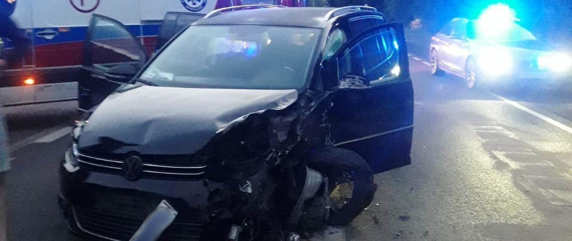 Samochód osobowy rozbity a w tle karetka Pogotowia ratunkowego.