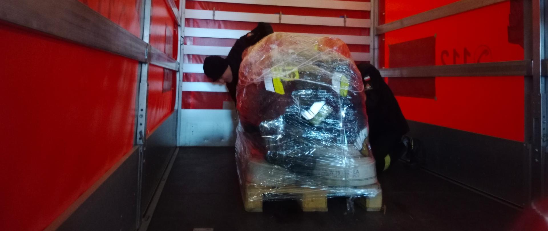 Zdjęcie przedstawia dwóch strażaków pakujących do samochodu dostawczego sprzęt dla ogarniętej wojną Ukrainy.