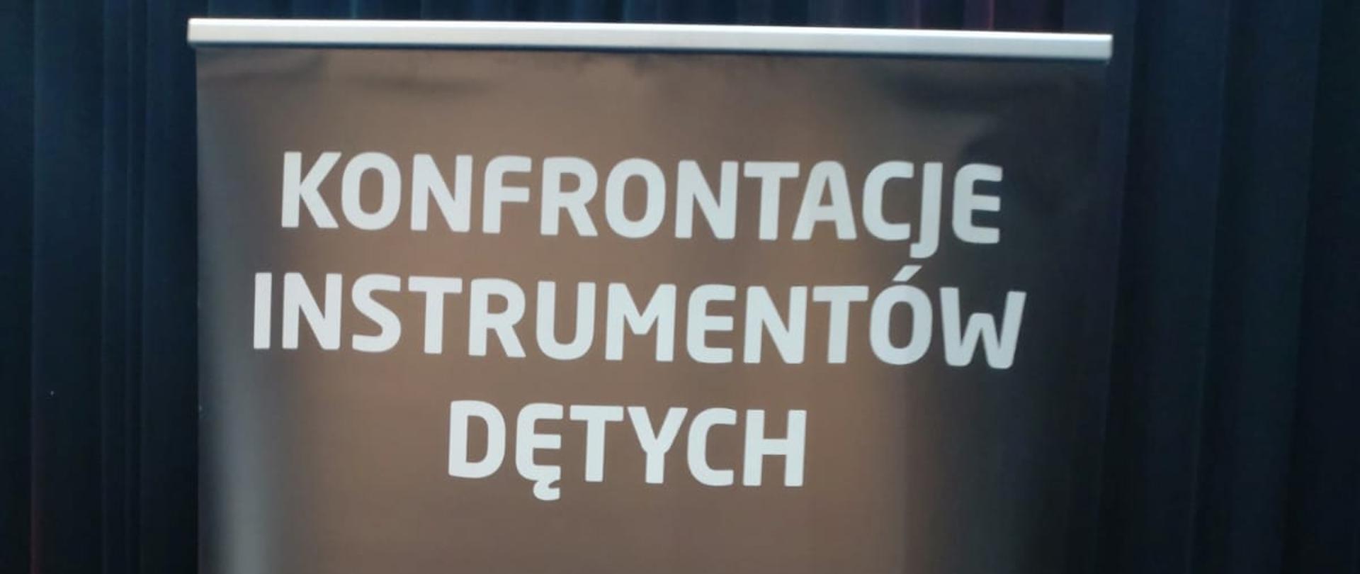 Uczeń Wit Jędrych z klasy klarnetu stoi na tle baneru konkursowego XXXII Konfrontacjach Instrumentów Dętych w Oławie 12-13 marca 2024 r. trzymając klarnet oraz dyplom