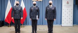 Fotografia przedstawia od lewej: st. bryg. Jarosława Nowosielskiego mazowieckiego komendanta wojewódzkiego, mł. bryg. Michała Gigołę zastępce komendanta powiatowego PSP w otwocku oraz bryg. Romana Krzywca komendanta powiatowego PSP w otwocku. Funkcjonariusze w umundurowaniu galowym. Na drugim planie godło Rzeczypospolitej Polskiej oraz flagi Państwowej.