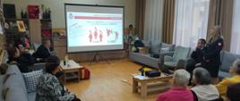 Sala wykładowa z seniorami w tle wyświetlana prezentacja o czadzie , burmistrz i funkcjonariusze PSP
