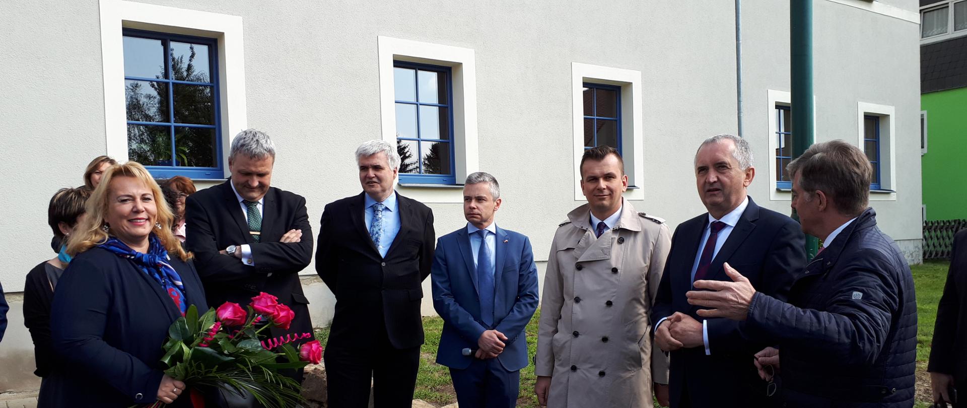 Na tle budynku stoi grupa ludzi. Wśród nich wiceminister Adam Hamryszczak