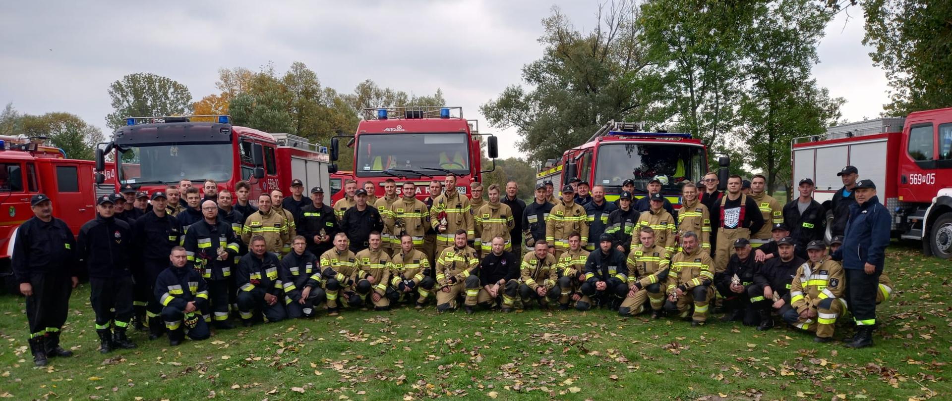 Zdjęcie grupowe uczestników manewrów, za nimi widoczne auta gaśnicze