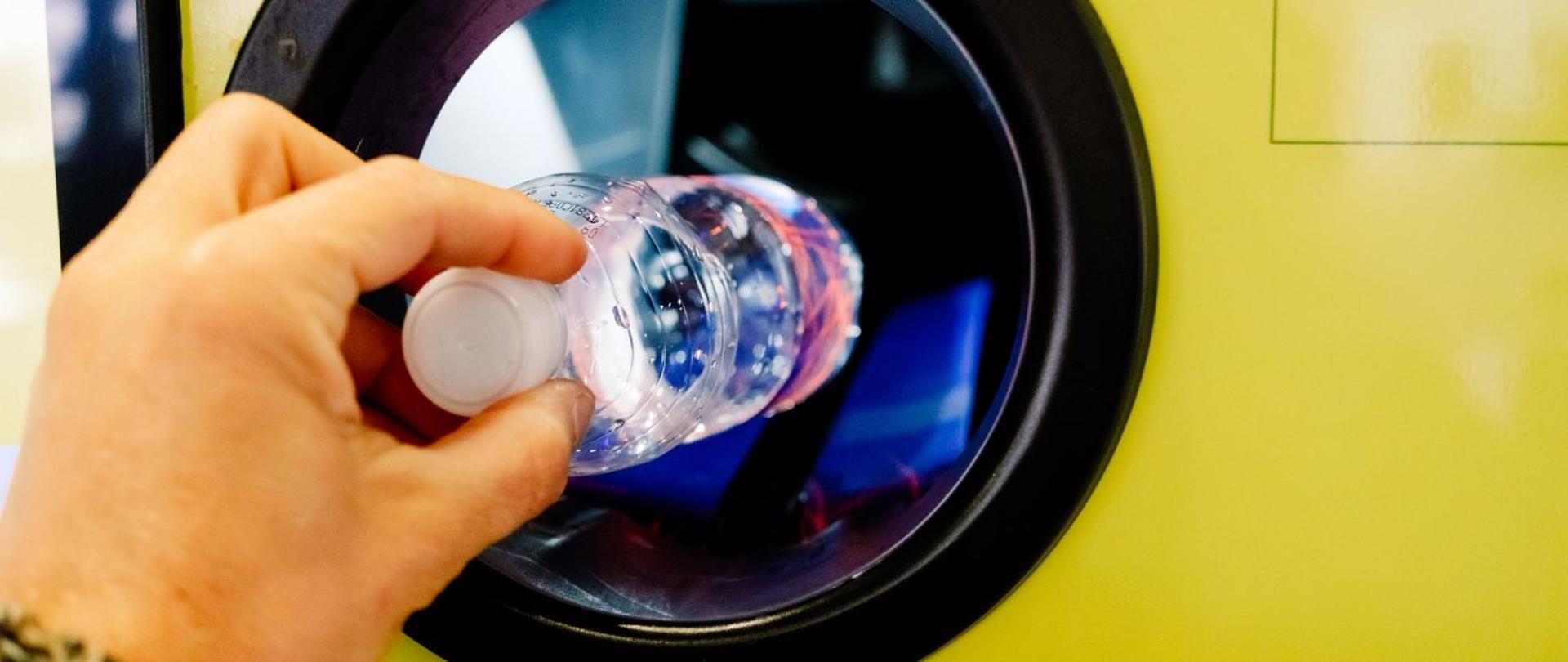 Mężczyzna wrzuca plastikową butelkę do automatu kaucyjnego.