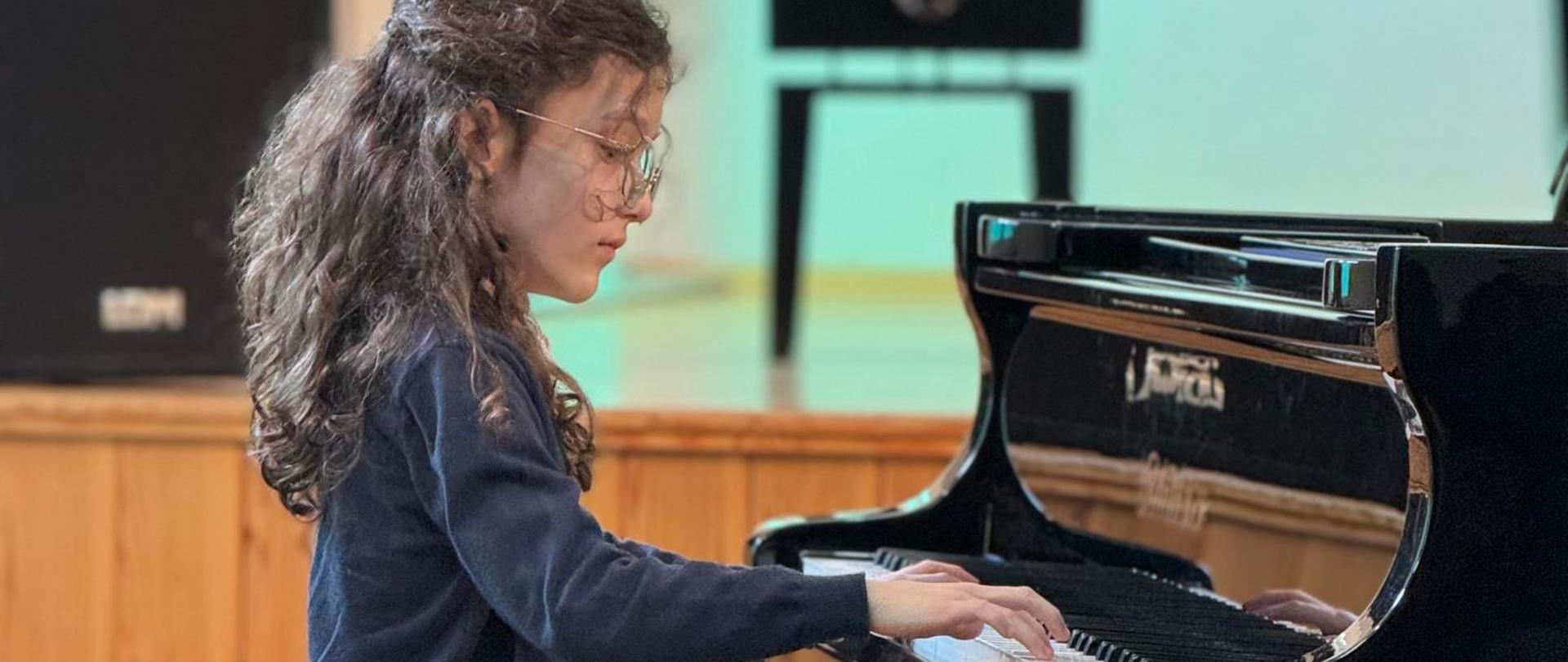 Zdjęcie przedstawiające jednego z wykonawców podczas koncertu w auli szkoły w dniu 11 marca 2024 roku.