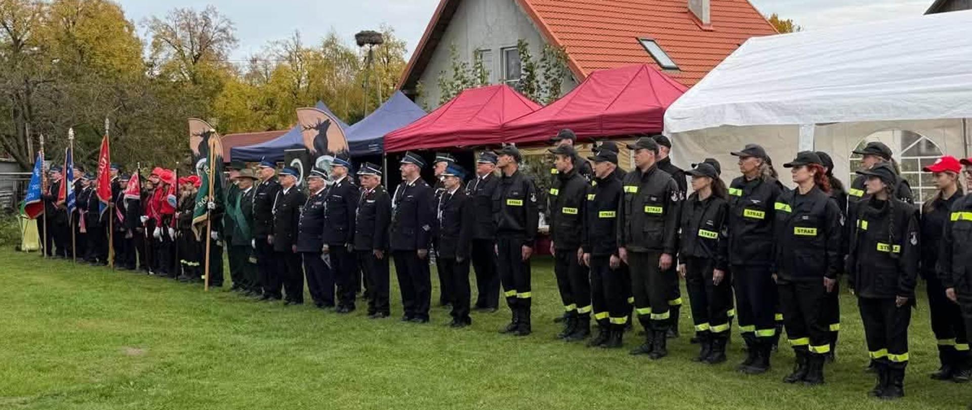 Przedstawiciele jednostek Ochotniczych Straży Pożarnych uczestniczą w uroczystym apelu zorganizowanym podczas wydarzenia strażackiego. W zbiórce biorą udział poczty sztandarowe, druhowie w mundurach wyjściowych oraz członkowie Młodzieżowych Drużyn Pożarniczych.