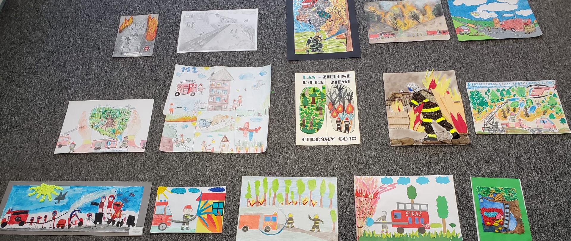 Zdjęcie przedstawia prace plastyczne namalowane przez dzieci na konkurs plastyczny, prace są położone na podłodze koloru szarego.
