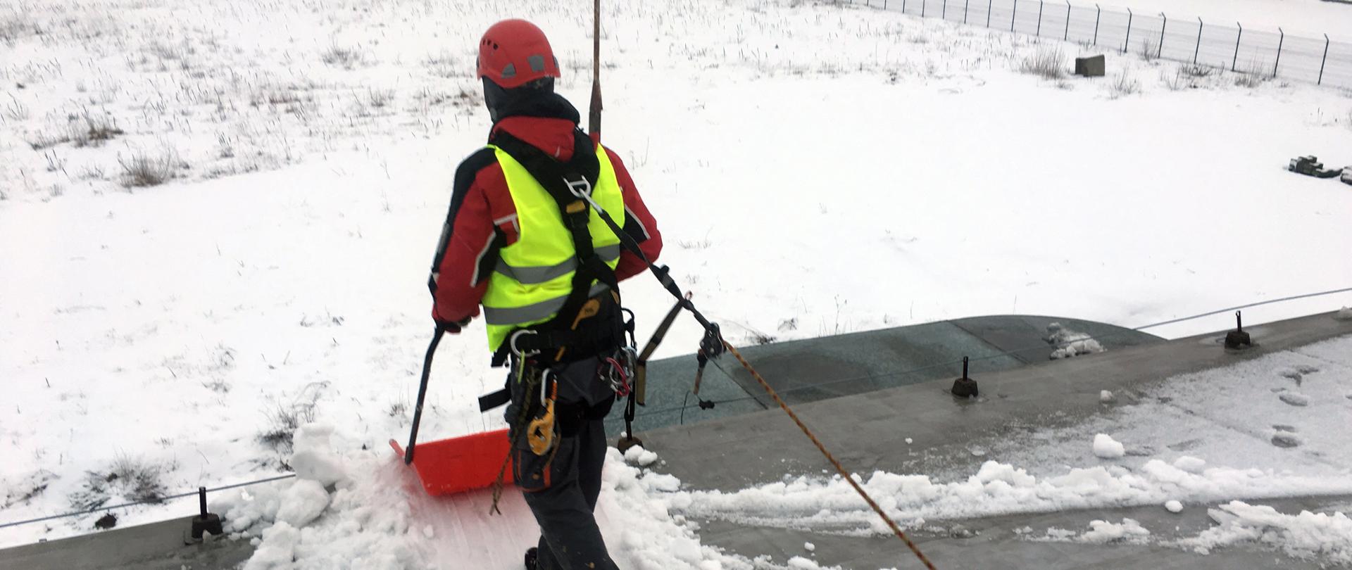 Zdjęcie przedstawia usuwanie śniegu z dachu budynku