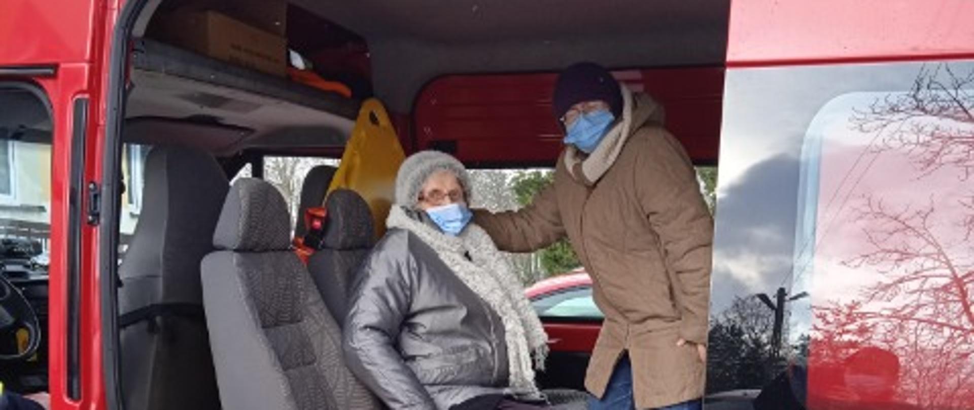 Zdjęcie przedstawia samochód pożarniczy. W środku dwie osoby przygotowane do transportu.