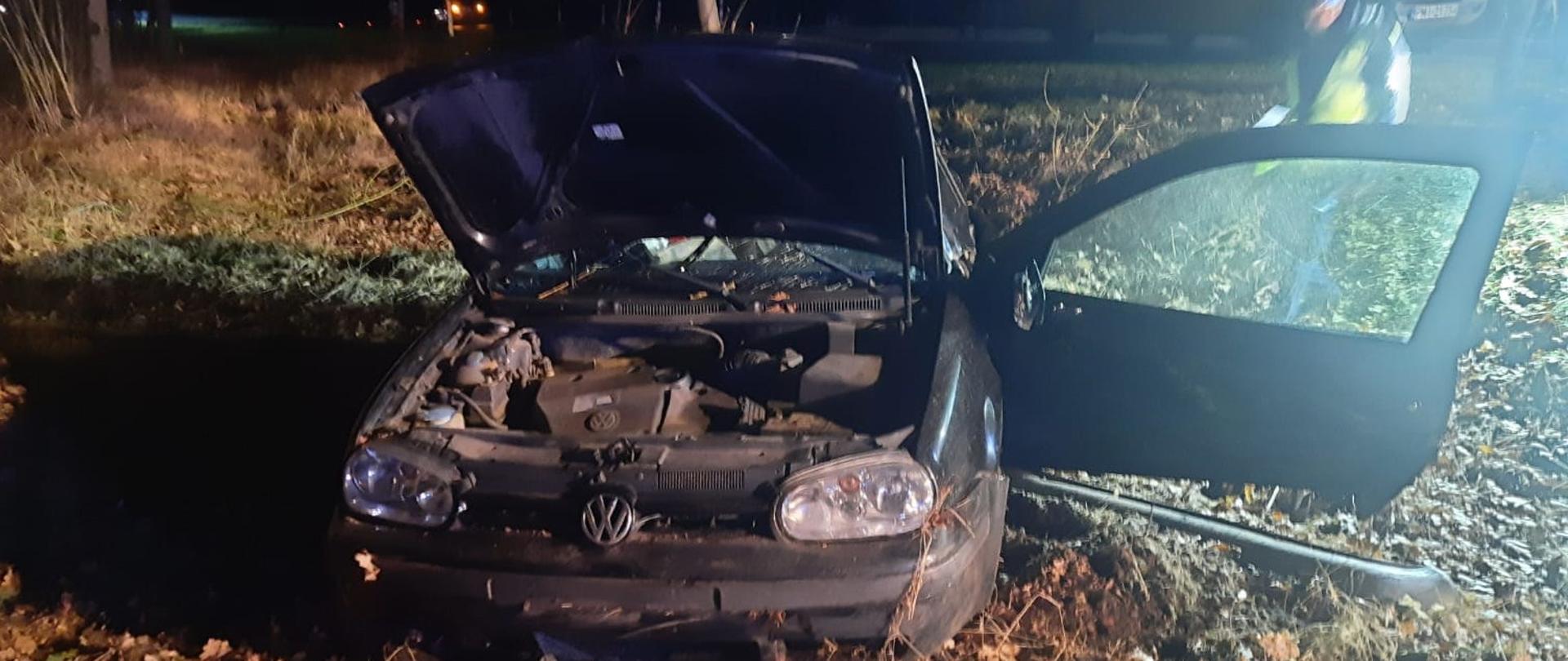 Czarny samochód w lesie, podniesiona maska, otwarte lewe drzwi, jest ciemno