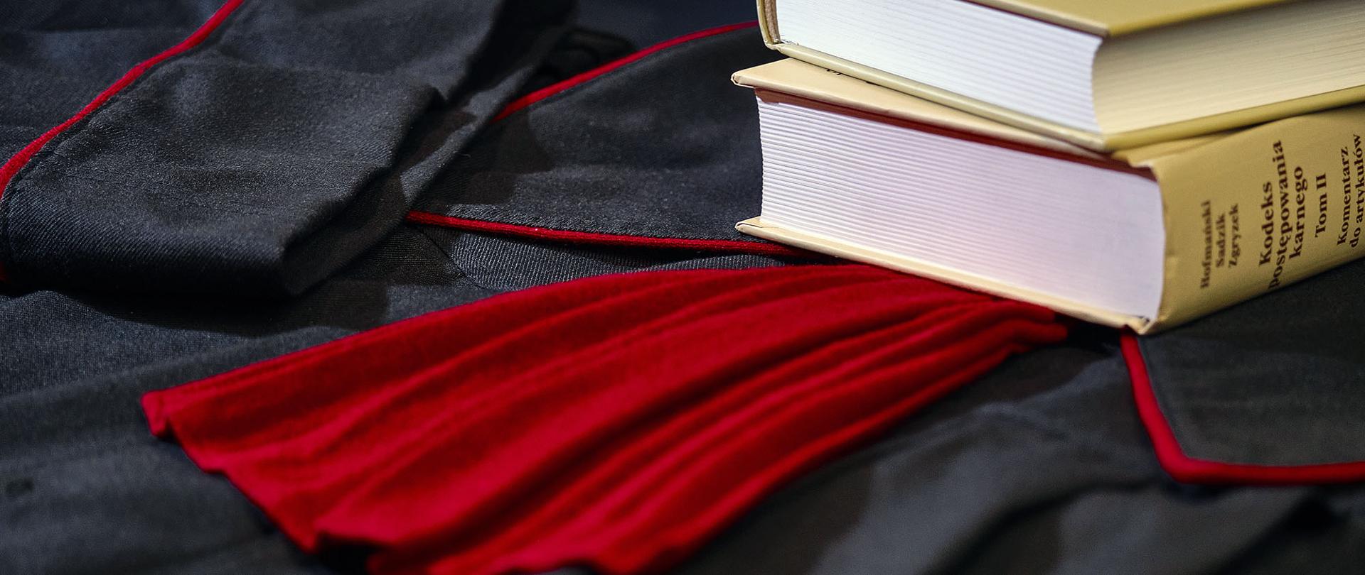 Na zdjęciu toga prokuratorska - czarna szata z czerwonym krawatem, a na niej ułożone na sobie egzemplarze komentarza do kodeksu postępowania karnego