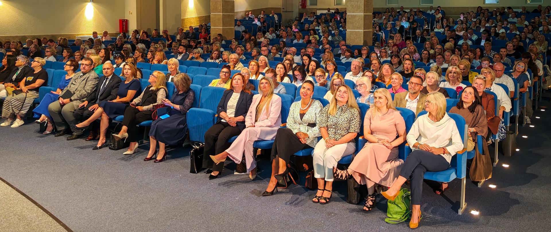 Uczestnicy konferencji siedzą na niebieskich fotelach w auli 