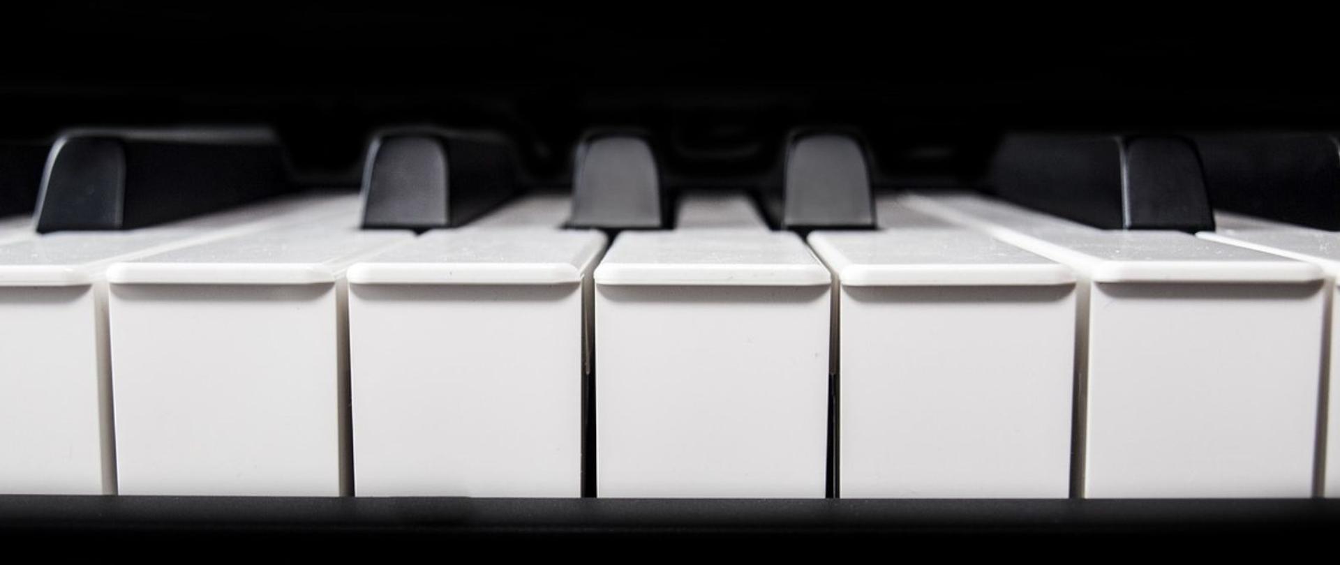 Plakat w pionie informujący o popisie uczniów klasy fortepianu p. Aliny Skupińskiej, który odbędzie się 20.05.2025r. o godz. 18.00. Plakat w kolorystyce czarno-białej. Po środku plakatu klawiatura fortepianu na czarnym tle. U góry z lewej strony logo szkoły oraz nazwa. Na dole data i godzina wydarzenia.