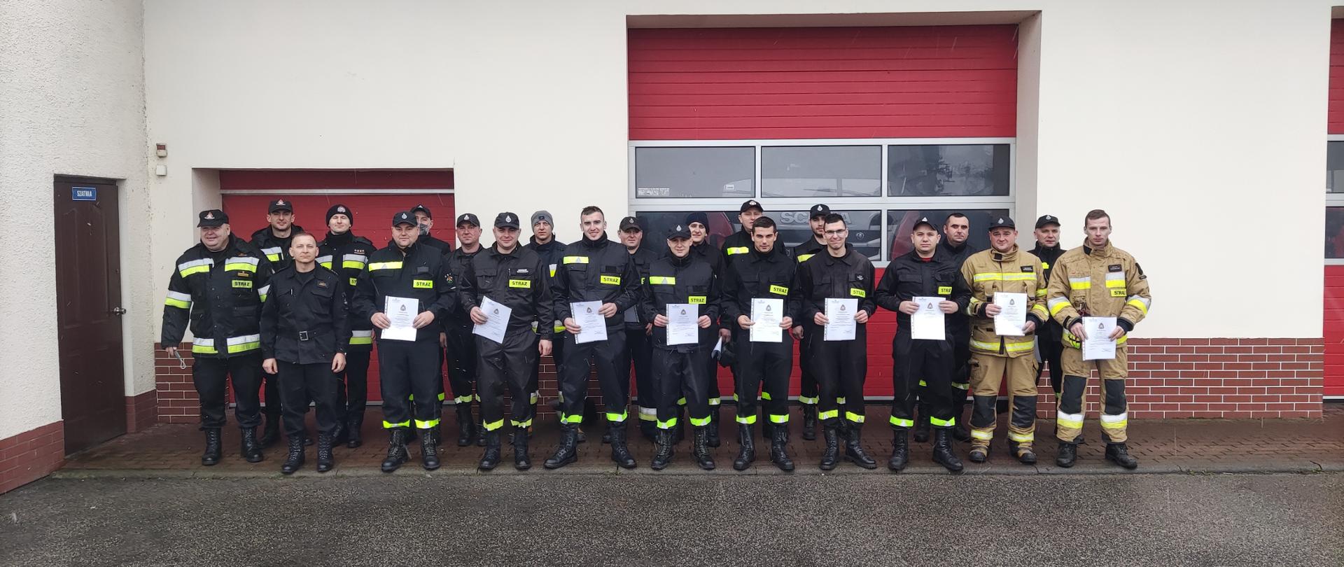 Zdjęcie przedstawia strażaków PSP i OSP z dyplomami ukończenia szkolenia kursu kierowców konserwatorów sprzętu ratowniczego osp na tle garaży jednostki ratowniczo-gaśniczej KP PSP w Radziejowie