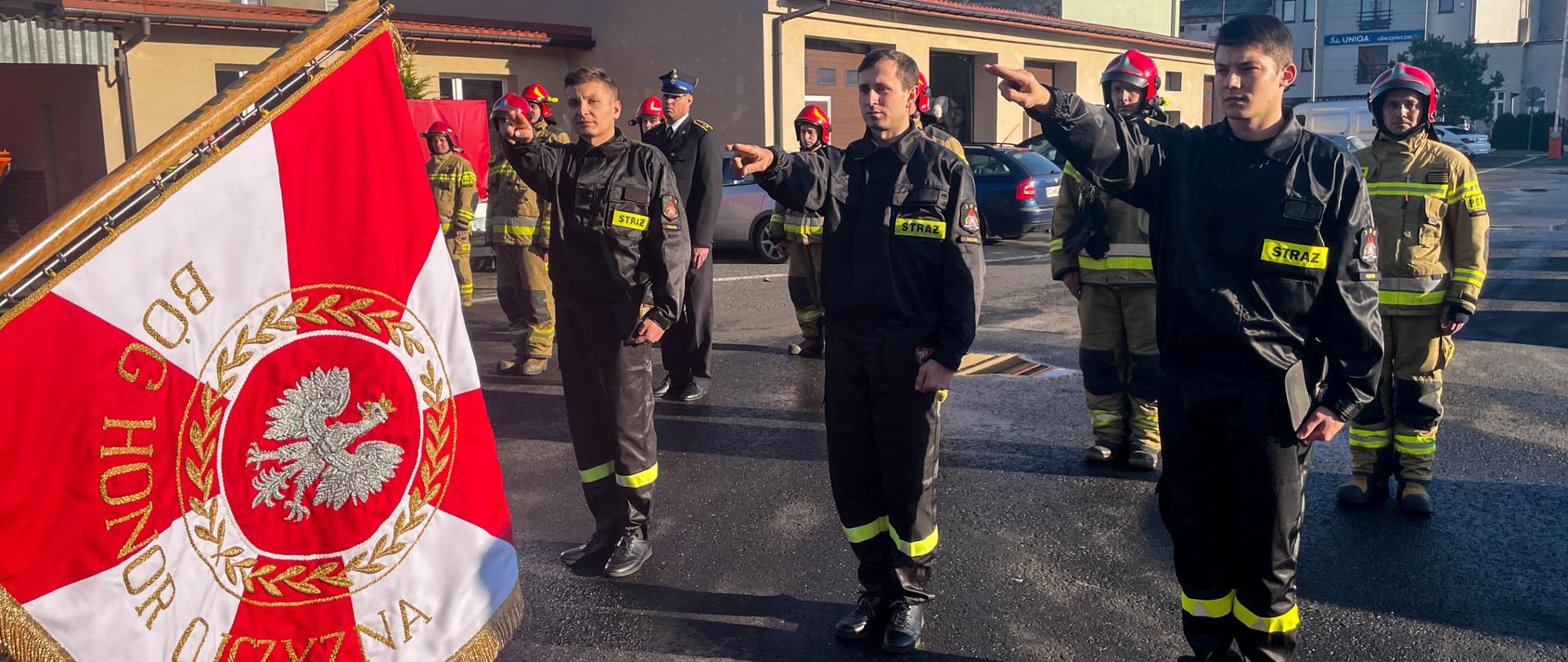 Zdjęcie przedstawia plac komendy na którym zgromadzeni są strażazcy ustawieni w szergu, a na ich przodzie trzech strażaków którzy ślubują przed sztandarem komendy
