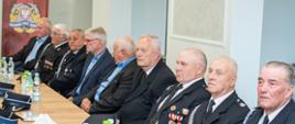 Seniorzy pożarnictwa siedzą w mundurach OSP za stołem
